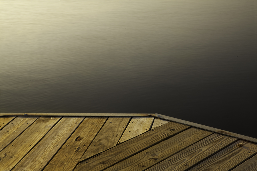 This Brian Charles Steel photo depicts Lake Prien in Lake Charles, Louisiana. The shot is facing the dock and downward angle.  The dock fills up the bottom third of the frame.  Starting at the left side it comes two thirds of the way across and then turns its angle downward towards the bottom right corner. The lake fills the rest of the frame.  The water closest to the dock is dark.  The farther away from the dock the water is the lighter it becomes. 